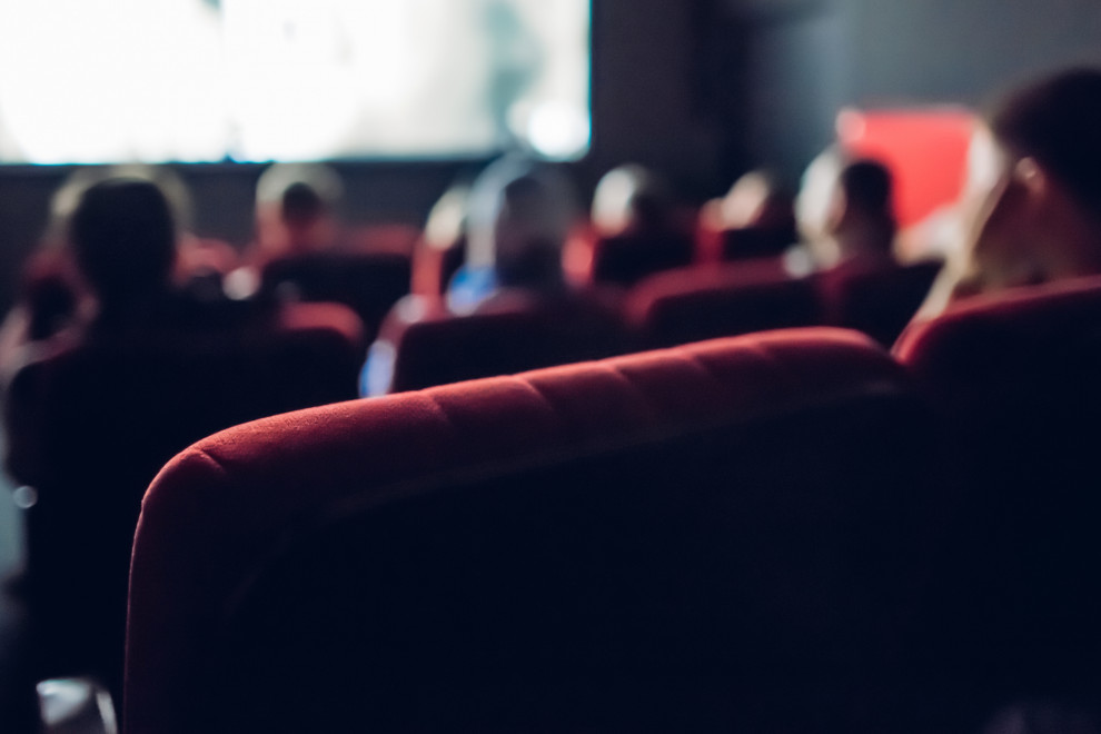 Pogled iz zadnje vrste kinematografa na nekaj obiskovalcev filmske projekcije in na platno