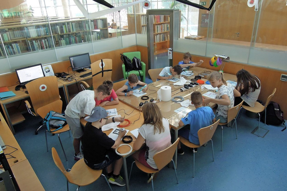 Mladi okrog skupne mize ustvarjajo na Mojstrovalnici v Goriški knjižnici Franceta Bevka. 