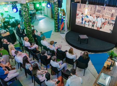 People are sitting in the Slovenian House and watching a documentary film about Leon Štuklje, which is shown on the big screen in front of them.