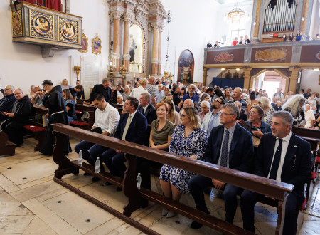 Udeleženci slovesnosti ob vrnitvi oltarne slike sedijo v klopeh piranske samostanske cerkve sv. Frančiška