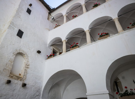 Dvoriščna bela grajska fasada z dvema obokanima balkonoma, na ograjah katerih so podolgovati lonci rdečih svetlic