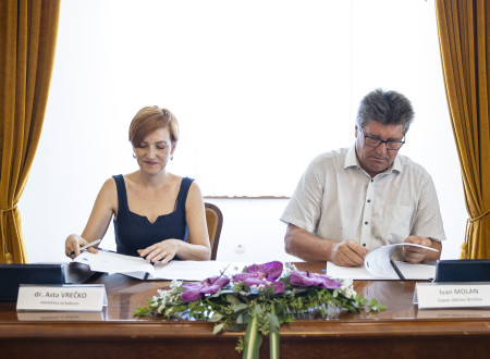 Ministrica in župan sedita za mizo in podpisujeta pogodbo
