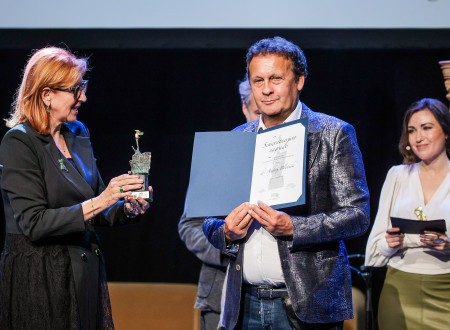 Dobitnik nagrade v rokah drži razprto modro mapo s plaketo