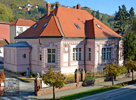 Neobaročna zgradba z roza fasado in razgibano zunanjostjo, del katere so štirje vogalni stolpiči, baročne kartuše in dekorativni zaključki stavbe