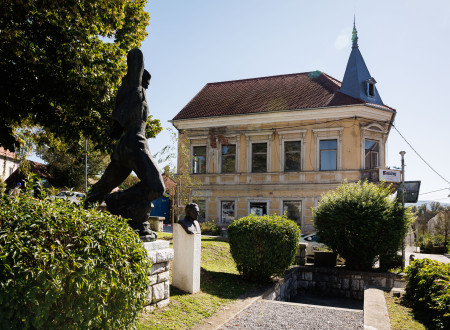 Stavba propadajoče meščanske hiše, pred njo park, v katerem sta kip Belokranjskega partizana in doprsni kip maršaka Tita 