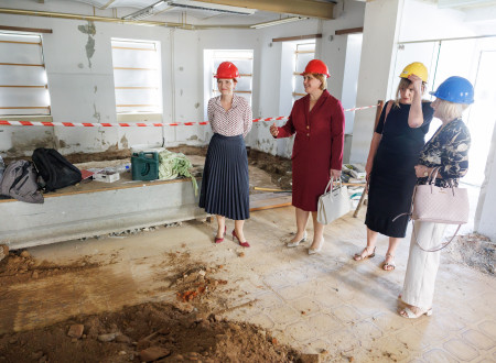 Ministrica in županja si v spremstvu dveh žensk, vse imajo na glavi čelado, ogledujejo notranjost zapuščene nekdanje meščanske hiše Konzum