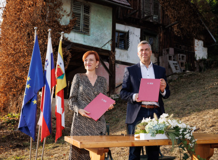 Nasmejana ministrica za kulturo in župan stojita pred zidanico in v rokah držita mapi s podpisanima izvodoma pogodbe o financiranju