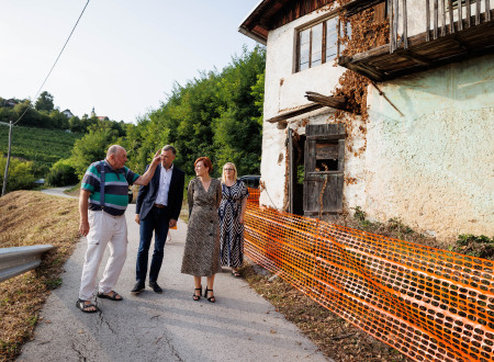 Ministrici in županu starejši gospod nekaj razlaga in kaže ob ogledu zunanjosti zidanice 