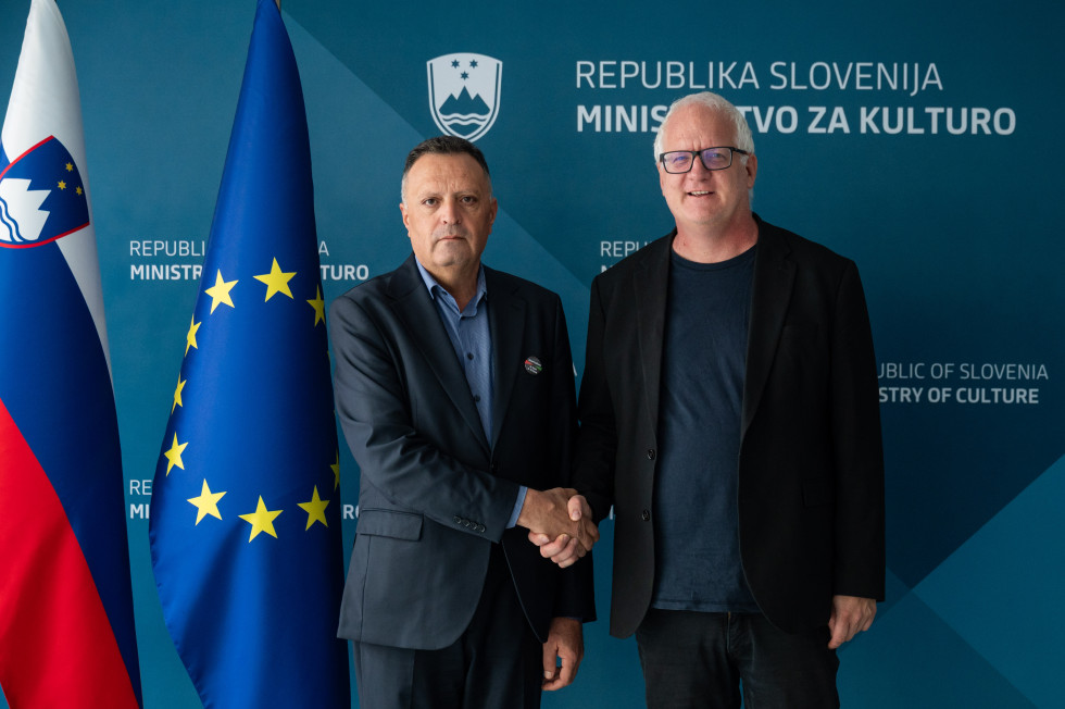 Predsednik Palestinskega novinarskega sindikata in državni sekretar se rokujeta, v ozadju modro ozadje z logotipom Ministrstva za kulturo ter zastavo Evropske unije in Slovenije