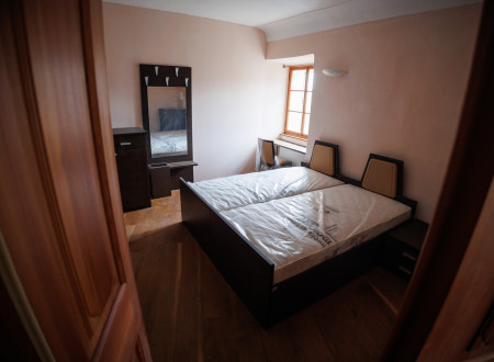 Soba z zakonsko posteljo, ob postelji okno, pred oknom polica, ki služi kot miza, s stolom, ob steni ogledalo, obešalniki in predalnik 