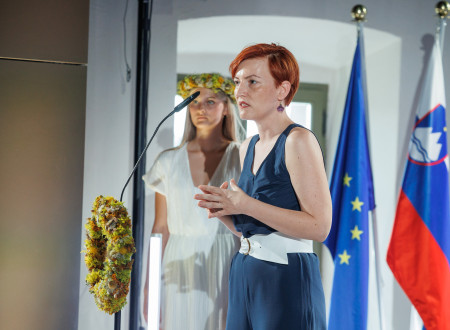 Ministrica za kulturo stoji pred mikrofonom in nagovarja zbrane