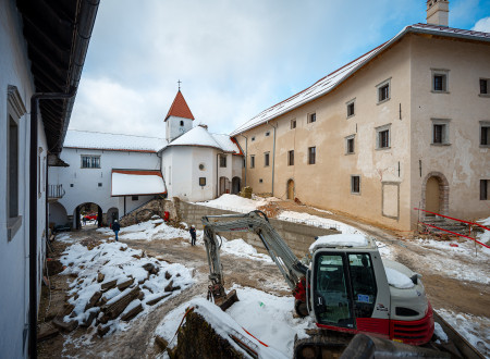Zasneženo dvorišče gradu, ki je v prenovi, na njem bager