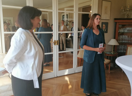 Veleposlanica in generalna direktorica med nagovorom, v ozadju steklena vrata z odsevom udeležencev predstavitve slovenske kandidature za Unescov Odbor za svetovno dediščino