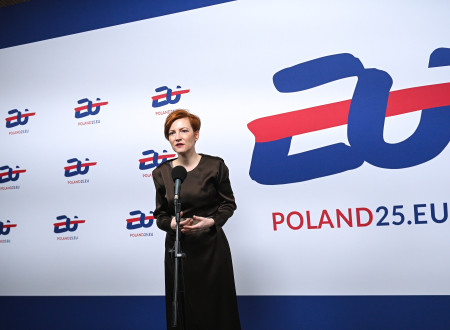 Ministrica za kulturo stoje govori v mikrofon, v ozadju stena z večimi logotipi POLAND25.EU