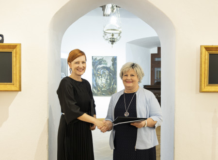 Ministrica za kulturo in županja stojita druga ob drugi pred obokano vratno nišo in se rokujeta