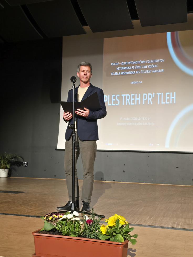 Državni sekretar stoji na odru pred mikrofonom, v rokah drži liste in nagovarja zbrane