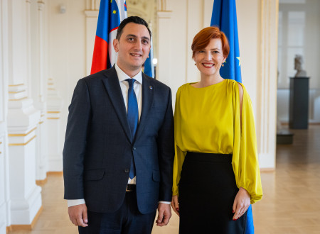 Nasmejana evropski komisar in ministrica za kulturo stojita drug ob drugem, v ozadju slovenska in evropska zastava