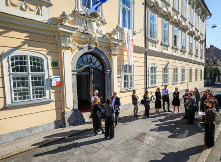 Osončena Gruberjeva palača, pred vhodom skupina ljudi stoji v polkrogu