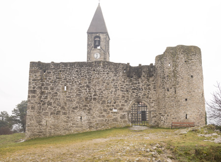 Obzidje z vhodom, izza katerega se dviga cerkveni stolp z nišo, v kateri je zvon, ter stolpno uro z uro