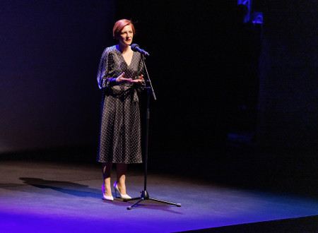 Ministrica za kulturo stoji pred mikrofonom na odru, ki je zatemnjen