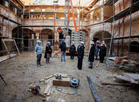 Skupina ljudi, med katerimi je ministrica za kulturo, stoji sredi notranjega grajskega dvorišča, ki je sredi obnove, okoli njega so gradbeni material in gradbeni oder.