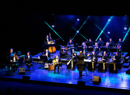 Džesovski orkester z dirigentom na  modro osvetljenem odru med igranjem