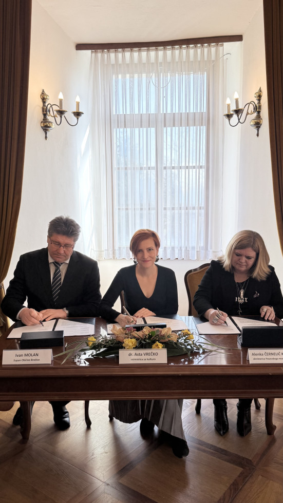 Župan, ministrica za kulturo in direktorica sedijo za mizo drug ob drugem in podpisujejo vsak svoj izvod pogodbe