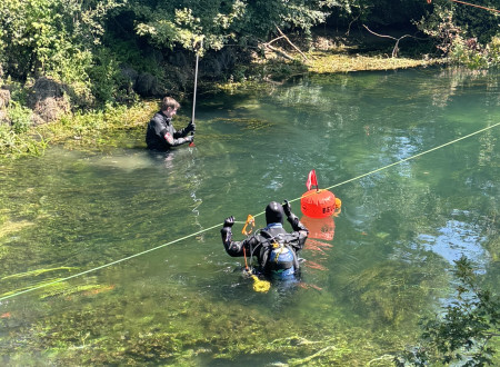 Tri osebe z opremo stojijo v plitvi reki.