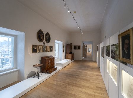 Svetel razstavni prostor s starinskima lesenima predalnikom in kredenco in starinskimi fotografijami na desni strani, na levi strani razlagalni panoji na steni