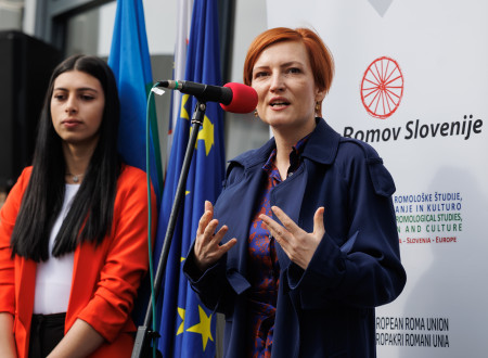 Ministrica stoji pred mikrofonon in nagovarja ljudi