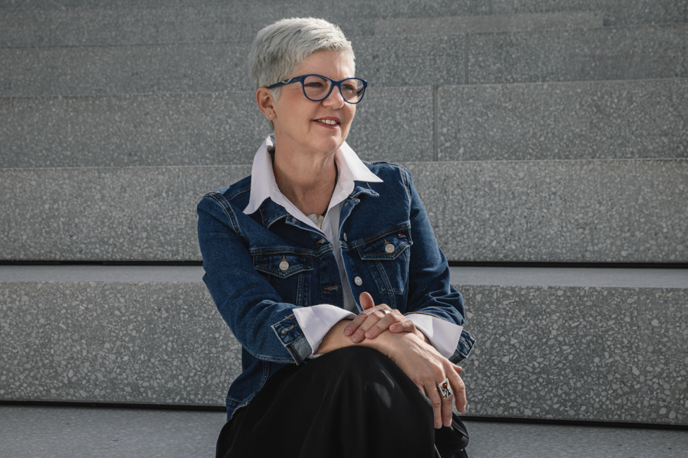 Direktorica sedi na sončen dan na stopnicah amfiteatra in zre rahlo v njeno levo stran