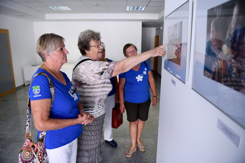 Klekljarice gledajo fotografijo, obešeno na razstavi v avli ministrstva 