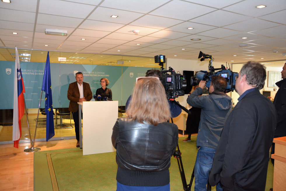 Minister in državna sekretarka, pred njima stojijo novinarji in sva televizijska snemalca