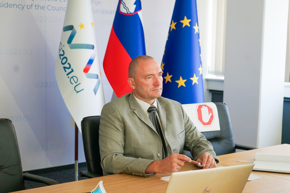 Minister v sivi obleki med sestankom sedi za mizo in spremlja dogajanje na računalniku 