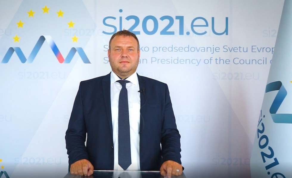 Moški stoji za govorniškim pultom, v ozadju je logotip slovenskega predsedovanja Svetu Evropske unije