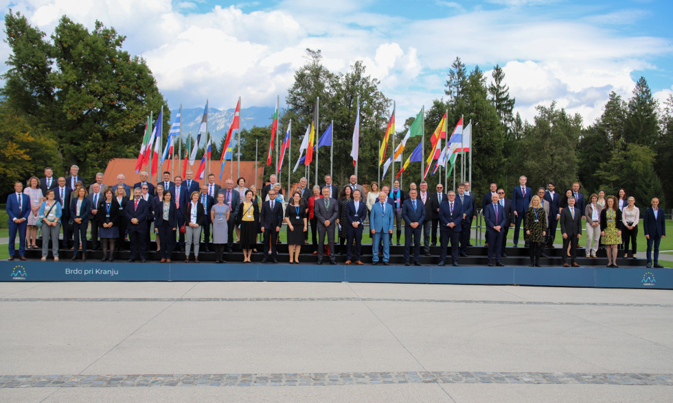Udeleženci sestanka stojijo na stopnicah v ozadju zastave držav članic Evropske unije