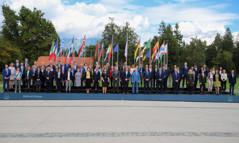 Members of the delegations standing on stairs. Behind them the flags of 27  EU member states