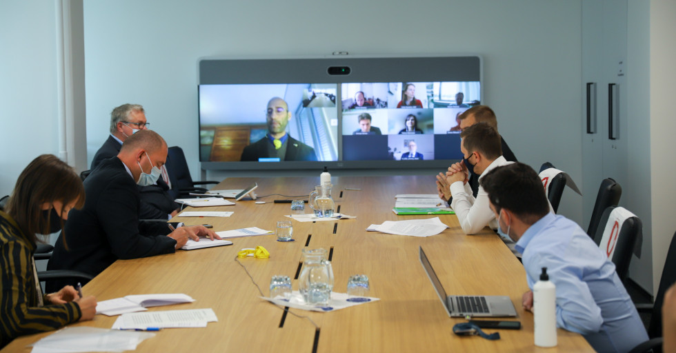 Minister sitting at the table with his coworkers. On a big screen in front of them the representatives of non govermental organizations. 