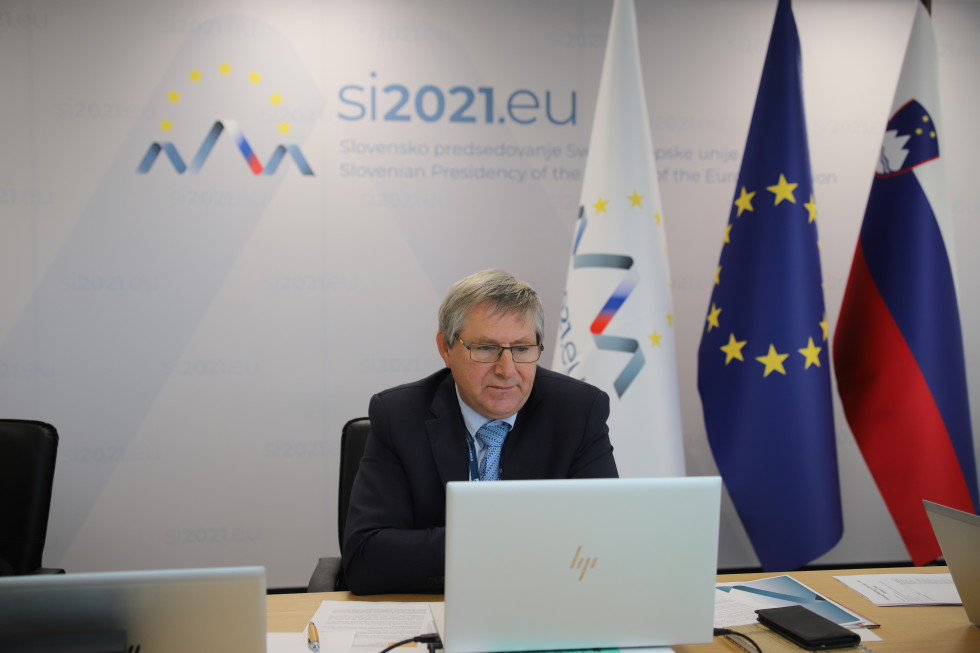 Generalni direktor sedi pred računalnikom v ozadju  zastave Predsedovanja Svetu EU, EU in Slovenije