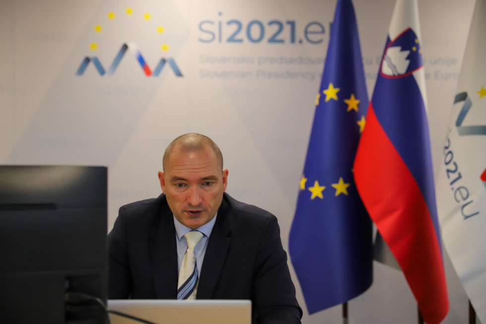 Minister govori v ekran. Za njih zastava Evropske unije in Slovenije