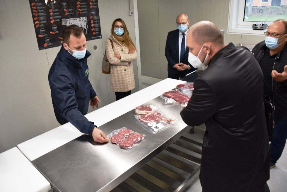 Minister si skupaj s predstavniki kmetije ogleduje mesne izdelke. Na mizi hamburgerji. 