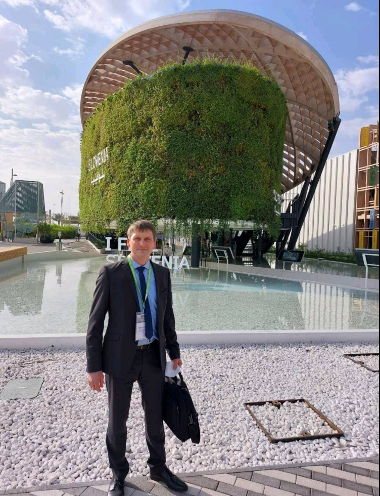 Državni sekretar stoji. Za njim slovenski paviljon na svetovni razstavi EXPO. 