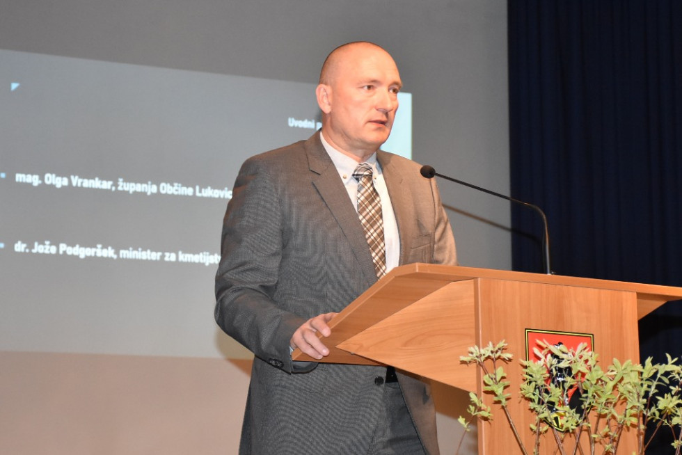 Minister stoji za govorniškim pultom. 