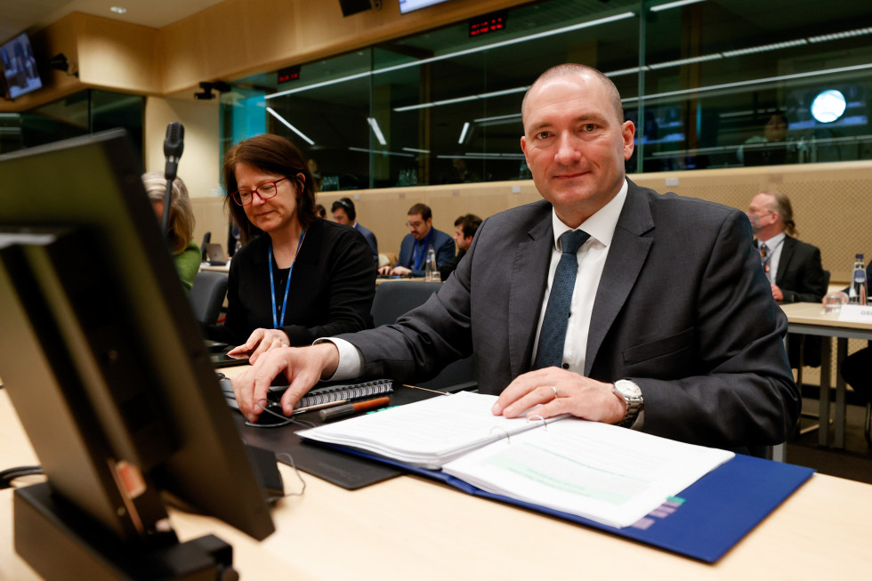 Minister sitting at his desk. In front of him a computer screen. 