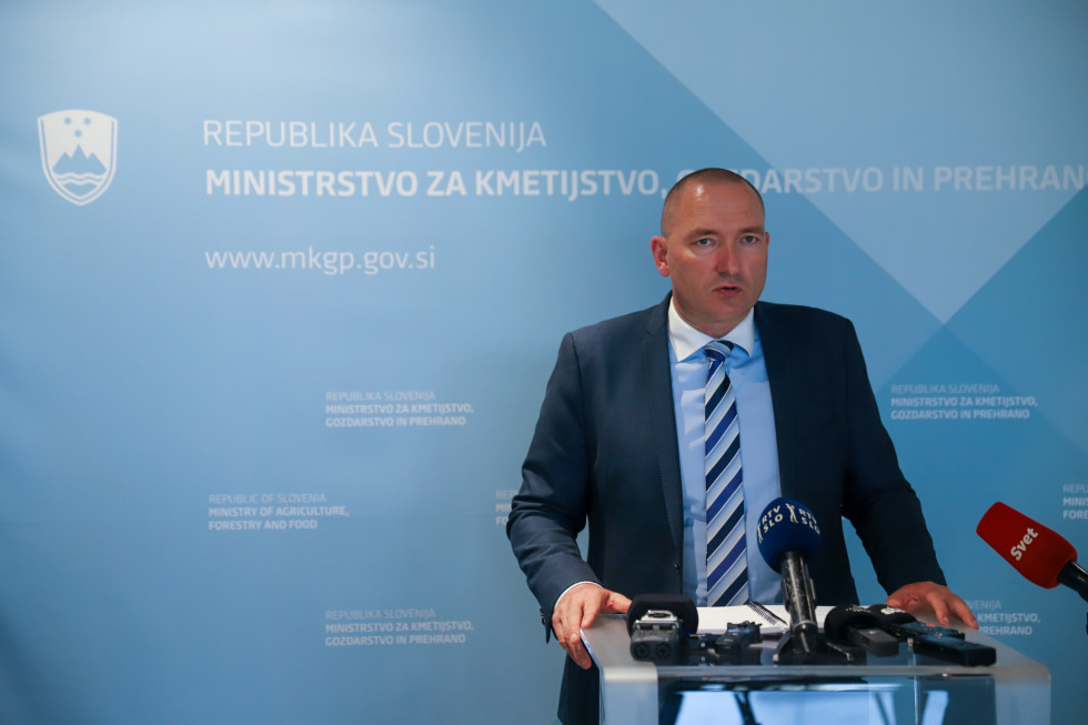 Minister stoji za govorniškim pultom med izjavo za medije.