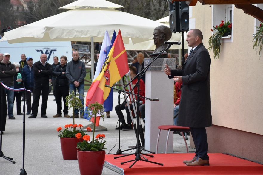 Minister stoji za govorniškim pultom in govori. 