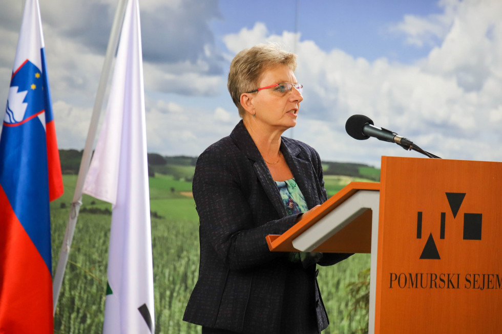 Ministrica stoji za govorniškim pultom in govori.