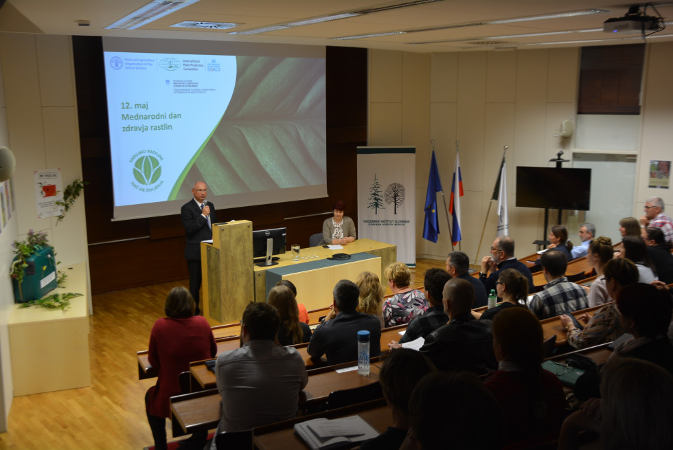 Predavalnica, na odru stoji državni sekretar in nagovarja udeležence posveta