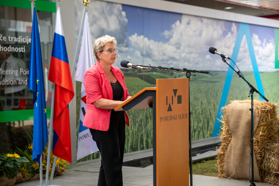 Ministrica stoji za govorniškim pultom in govori.