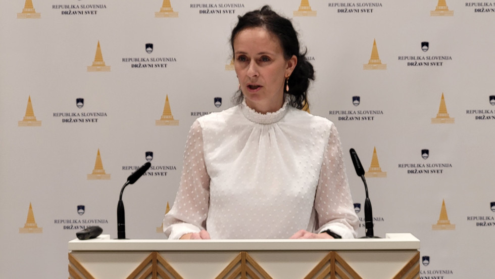 Vršilka dolžnosti stoji za govorniškim pultom in govori.